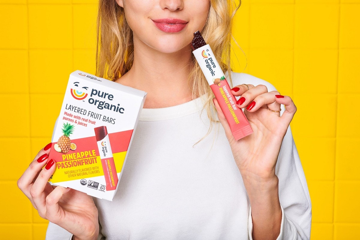 lady holding Pure Organic box and snack bar on a yellow background